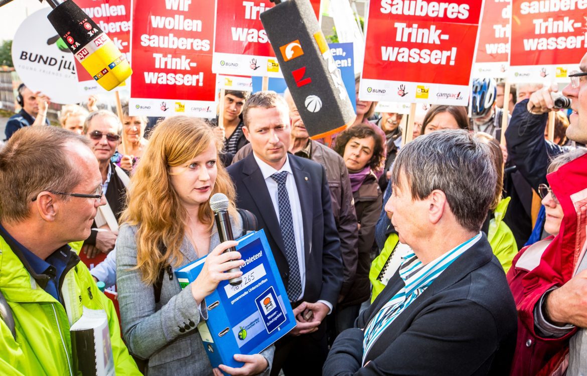 Referentin des Umweltinstitut München interviewed Sprecherin zu Fracking und ist von Demonstrant:innen umgeben.