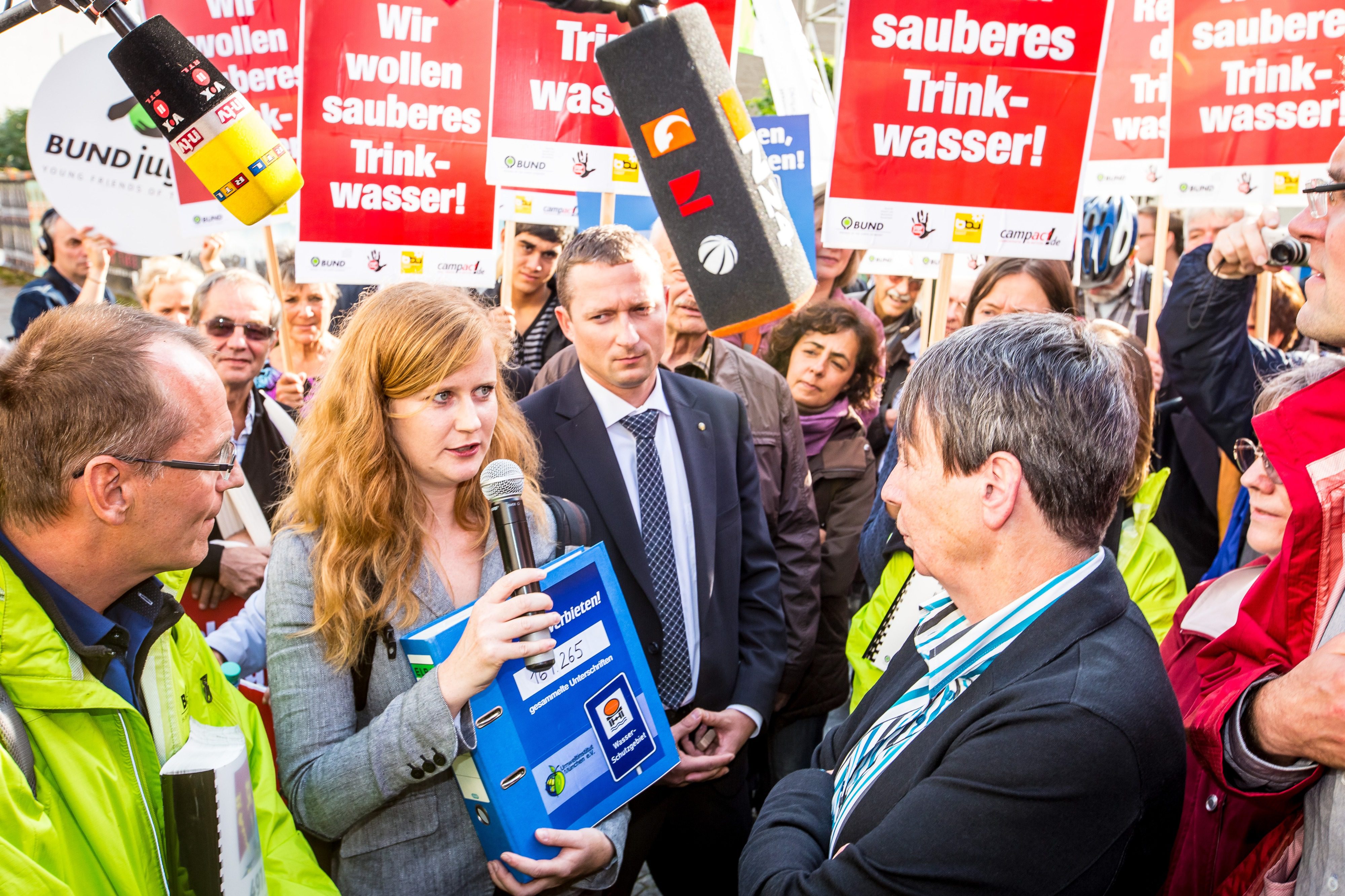 Referentin des Umweltinstitut München interviewed Sprecherin zu Fracking und ist von Demonstrant:innen umgeben.