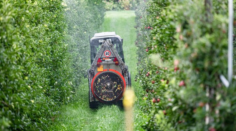 Traktor spritzt Pestizide in Apfelplantage