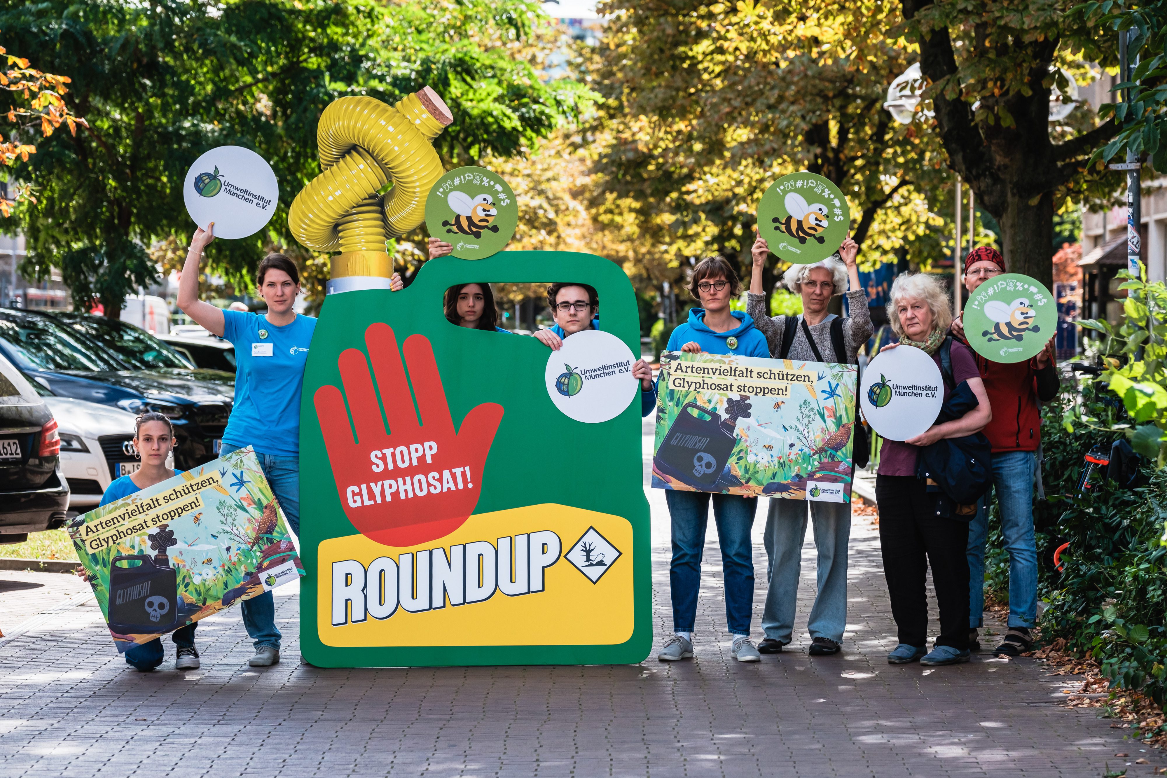 Das Team vom Umweltinstitut München bei der Übergabe-Aktion gegen Glyphosat in Berlin 2023 vor dem Landwirtschaftsministerium mit Protestschildern und einem übergroßen Roundup Kanister mit zugeknotetem Schauch