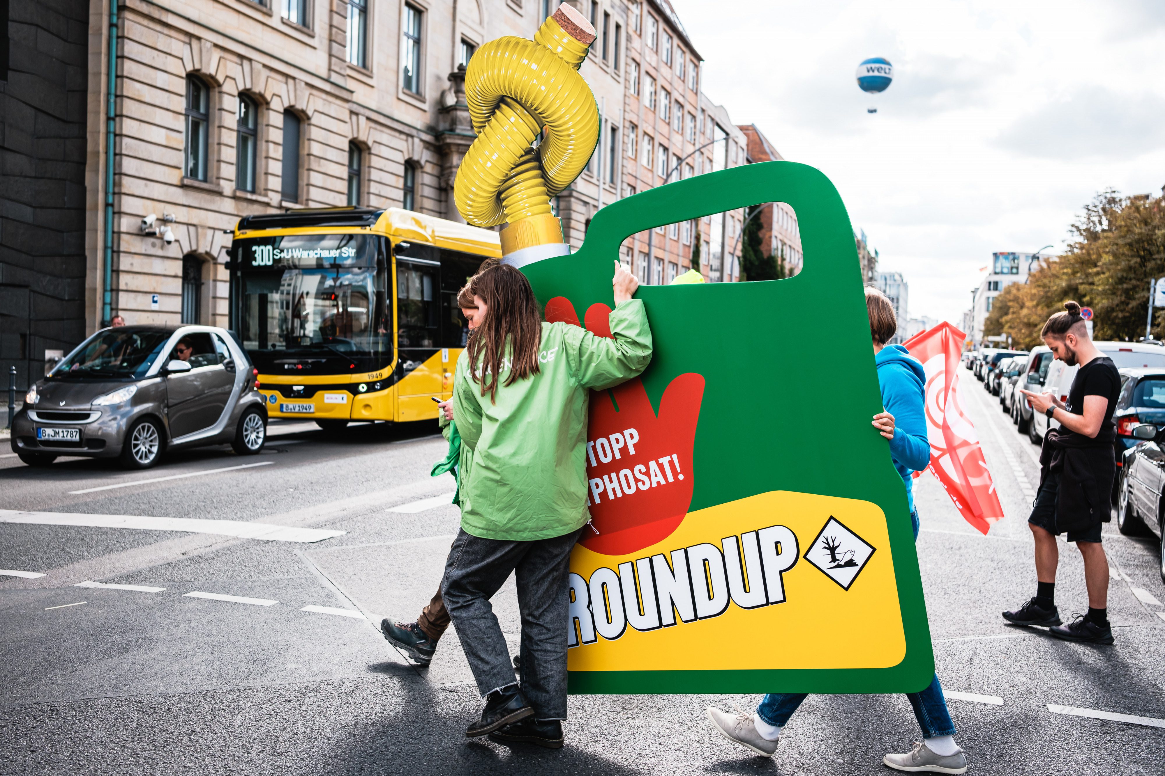 Transport eines übergroßen Roundup-Kanisters mit zugegknotetem Schlauch zu Fuß über die Straße zur Übergabe-Aktion in Berlin