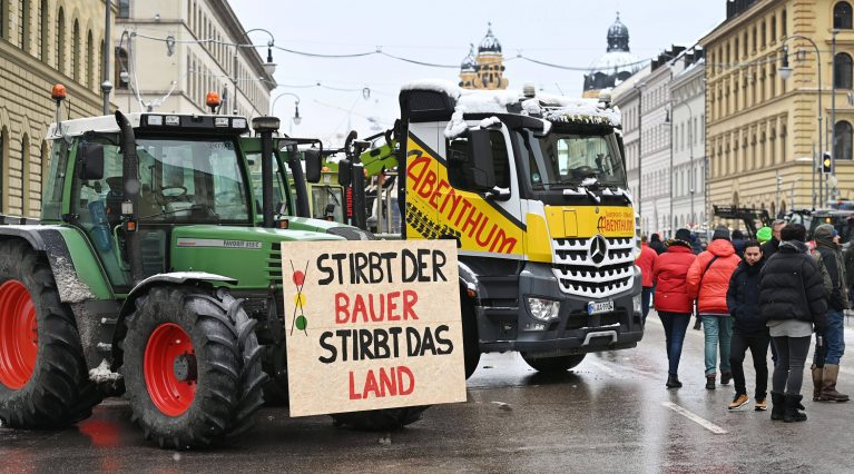 Vor einem gelben LKW präsentiert ein grüner Traktor das Schild 