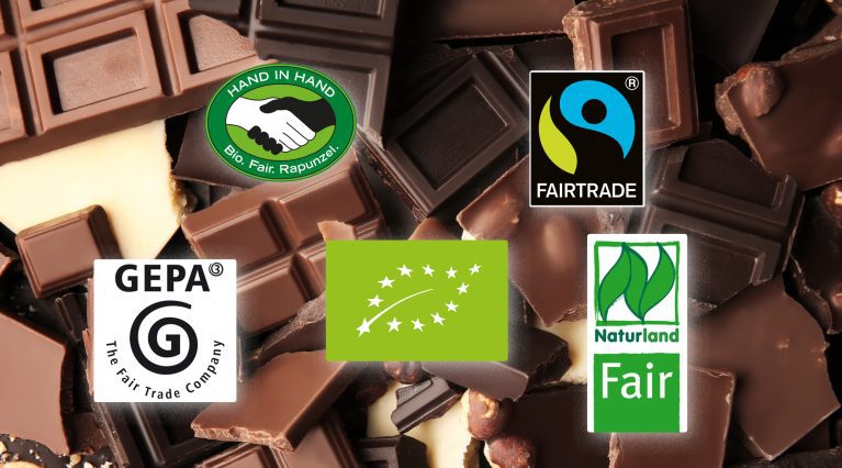 Schokoladenstücke mit verschiedenen Bio- und Fair-Trade-Siegeln, darunter Fairtrade, Naturland, EU-Bio, GEPA und Hand in Hand.