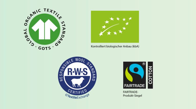 Vier Textilsiegeln: GOTS-Siegel (Global Organic Textile Standard), EU-Bio-Logo für kontrolliert biologischen Anbau, dem Responsible-Wool-Standard-Siegel sowie dem Fairtrade-Cotton-Produktsiegel.