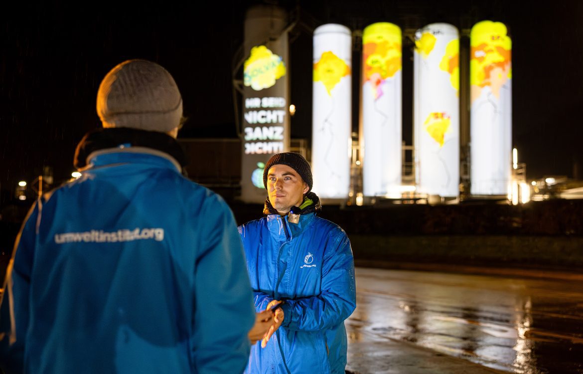 Klimateam des Umwetlinstituts vor der Projektion von Rissen und Spruch Ihr seid nicht ganz dicht auf Tanks der Solvay Chemiefabrik