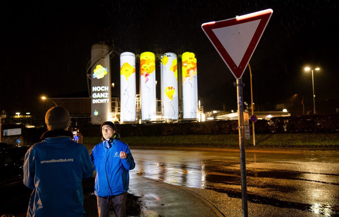 Klimateam des Umwetlinstituts vor der Projektion von Rissen und Spruch Ihr seid nicht ganz dicht auf Tanks der Solvay Chemiefabrik