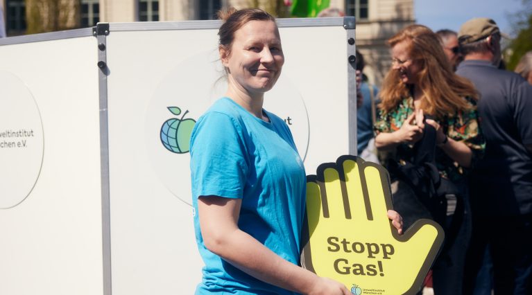 Person mit Umweltinstitut München T-Shirt auf einer Demo mit einem Schild 