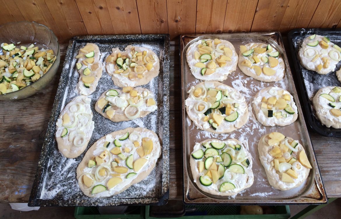 Auf zwei Backblechen liegen Teigfladen, die mit Gemüse belegt sind.